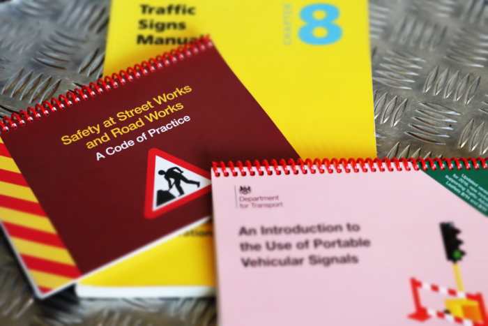 Large yellow training manual with 2 smaller ones on top. One features a men at work road sign